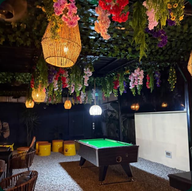 The lounge at Onijekuje Chopify, draped with hanging flowers and lanterns over a green pool table